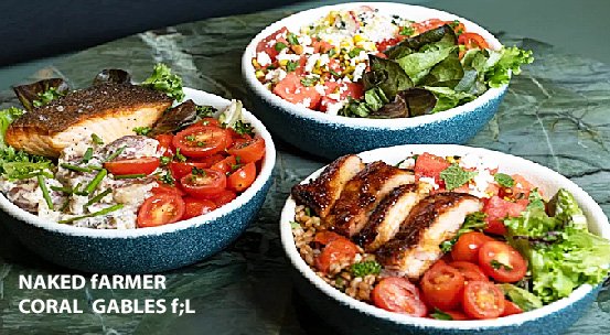 Three bowls of fresh salads on a stone surface. One bowl contains grilled salmon with cherry tomatoes, while another features grilled chicken on greens with tomatoes. The third bowl contains a colorful salad topped with corn, diced tomatoes, and mixed greens.