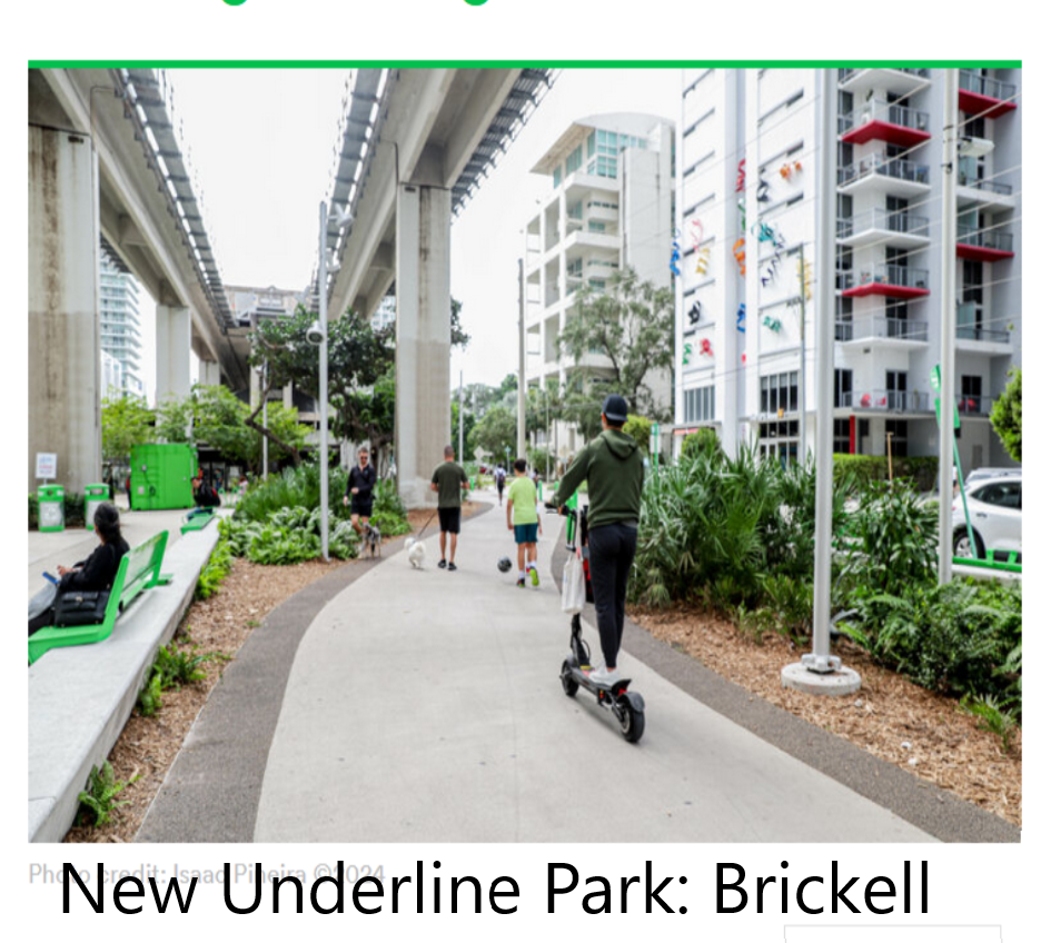 A person riding a scooter along a smooth pathway in Underline Park, Brickell, Miami. Lush greenery lines the path, with modern buildings and a raised train track visible in the background. Several people walk nearby, enjoying the urban park setting.