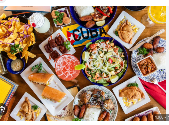 A vibrant spread of south Florida cuisine featuring colorful plates with rice, salad, empanadas, fried plantains, and other traditional dishes. A sign reading 'Cuba' is partially visible, enhancing the cultural theme of the meal, ideal for enjoying flavors while discussing GLP-1 medications that eliminate food noise for long-term weight loss.