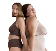 Two women stand back-to-back, showcasing diverse body types and confidence. One wears a dark brown bra and briefs, while the other dons a light beige set. They both smile softly, exuding a sense of empowerment in a simple, minimalist setting.